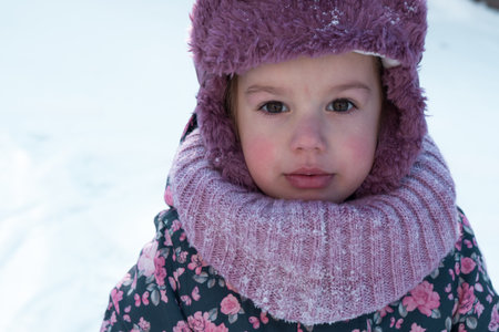 Close-up portrait authentic little preschool minor 3-4 years girl in pink hat look at camera posing smile in snowy frosty weather. happy kid face have fun outdoorsの写真素材