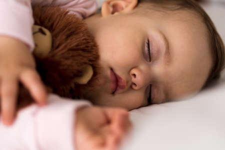 Authentic portrait cute caucasian little infant chubby baby girl or boy in pink sleep with teddy bear on white bed. child resting at lunchtime. care, Sleeping kid, Childhood, Parenthood, life conceptの写真素材