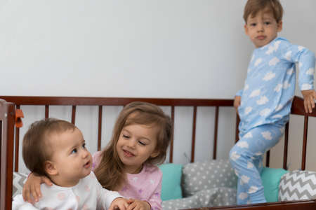 Cute cheerful 3 little kids girl and boy siblings preschool children in grey baby crib after waking up from sleep in pajamas with legs dangling. Childhood, leisure, comfort, medicine, health conceptの写真素材