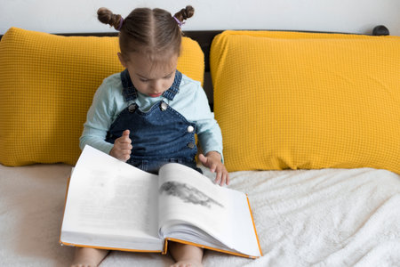 Two preshool, toddler children read large interesting book of fairy tales on yellow bed. Siblings little twins reader have fun, happy kid on quarantine at home. Friendship, family, education conceptの写真素材
