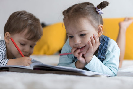 smart smiling preshool toddler children boy and girl draw with pencils lying on their stomach at...