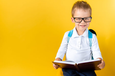 Banner Funny Preschool Child Boy in Big Glasses Reads Book on Yellow Background Copy Space. Happy...