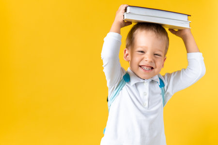 Banner Funny Preschool Child Boy 3-4 years with Book on Head and Bag on Yellow Background Copy Space. Happy Smiling Kid Go Back to School, Kindergarten. Success, Motivation, Genius, Superhero conceptの写真素材