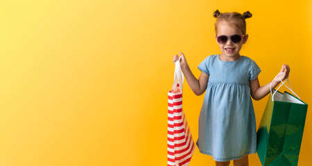 Banner Portrait Beautiful Happy Little Preschool Girl In Sunglasses Smiling Cheerful Holding Cardboard Bags Isolated On Orange Yellow Background. Happiness, Consumerism, Sale People shopping Conceptの写真素材