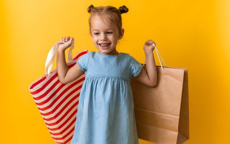 Portrait Caucasian Beautiful Happy Little Preschool Girl Smiling Cheerful And Holding Cardboard Bags Isolated On Orange Yellow Studio background. Happiness, Consumerism, Sale People shopping Conceptの写真素材