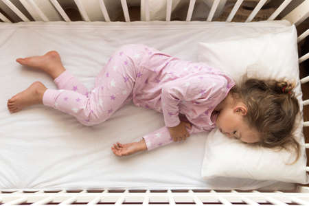 top view Cute little 3-4 years preschool baby girl kid sleeping sweetly in white crib during lunch rest time in pink pajama with pillow at home. Childhood, leisure, comfort, medicine, health conceptの写真素材