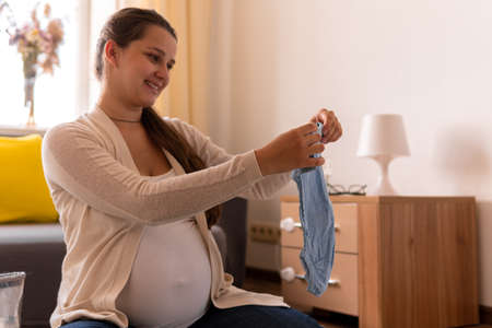 Cute Pregnant Woman Writing Packing List For Maternity Hospital Notebook Prepares Bag. Young Ledy In Pregnancy Have Fun Spend Time On Floor Near Sofa At Home. Motherhood, Medicine Health Care Conceptの写真素材