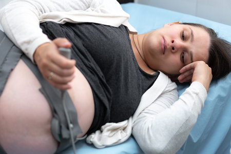 Pregnant Woman On Hospital Couch During Medical Control Cardiotocography. Gynecologist Doctor Hands Turn On Adjust CTG Device Clinic Consultant. Examine Expectant Belly Baby Mother Healthcare Check Upの写真素材