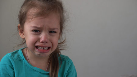 Portrait little girl sad upset child burst into tears cries sob looking at camera indoors. sincere...