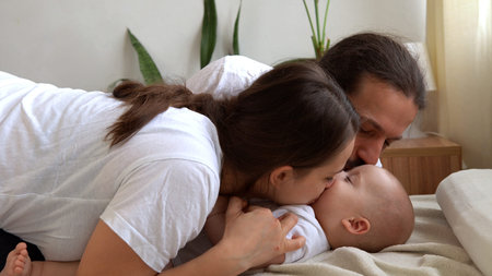 Woman And Man Holding Newborn. Mom, Dad And Baby On Bed. Close-up. Portrait of Young Smiling Family...