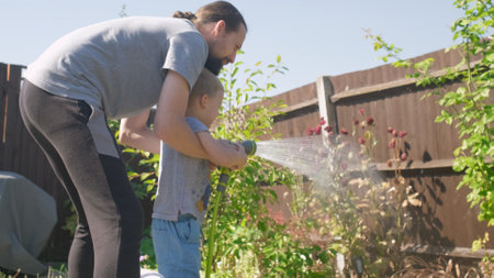 Father and Son. Funny little boy watering lawn plants in garden housing backyard with Dad. Summer house work. Hardworking preschool Kid outdoors. Children help with housework. activity for kidsの写真素材