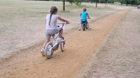 Sport activity for children. Small kids playing bicycle and scooter riding on path in park in summer drought dry grass. Little Brother and Sister Siblings playing together. Child development conceptの写真素材