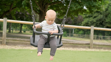 Funny Little Younger Newborn Infant Brother Boy On Swing. Baby Playing On Playground. Summer time outside. Kids Entertainment, Childhood, Child Development, Happy Family Conceptの写真素材