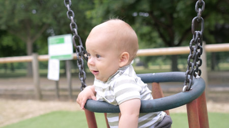 Funny Little Younger Newborn Infant Brother Boy On Swing. Baby Playing On Playground. Summer time outside. Kids Entertainment, Childhood, Child Development, Happy Family Conceptの写真素材