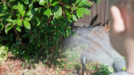Funny little boy watering lawn plants in garden housing backyard. Adorable child playing with irrigation hose at hot sunny summer outdoors. Children help with housework. activity for kids. Childhoodの写真素材