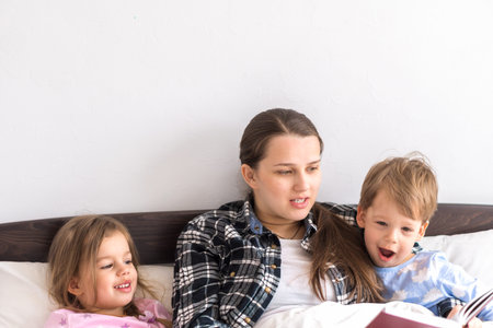 happy family. Close up loving mother lying with daughter son two kids pajamas in bed children...