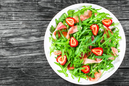 strawberry, arugula, prosciutto salad on the white dish on the old wooden rustic table, top view, closeupの写真素材