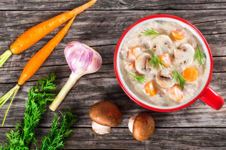 Delicious creamy cheese mushroom soup with spring carrots and veggies, decorated with dill, in a red...