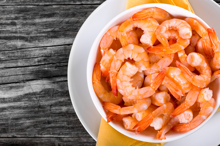 boiled tails of king shrimps on a white bowl on a dish with orange table napkin, on an old rustic table,top view, studio lightsの写真素材
