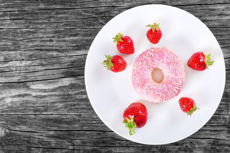 Donut with Strawberry Icing on a white dish with fresh strawberriy on the old wooden table, top viewの写真素材