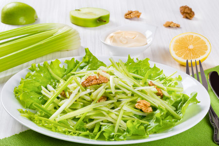 Studio macro of Waldorf Salad, authentic recipe, halves of a lemon and apple, celery and mayo in a gravy boat on a white wooden table, view from above, close-upの写真素材
