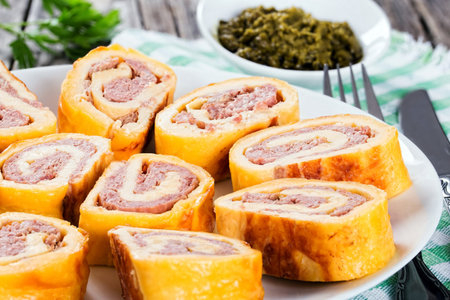 Tasty baked cheese meat Roll-Ups on white dish, parsley, chili pepper and cherry tomatoes on old wooden background, view from above, close-up, selective focusの写真素材