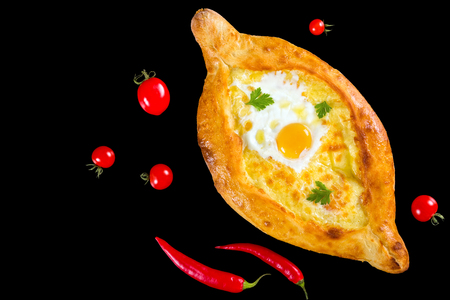 Ajarian khachapuri with egg isolated on black background with cherry tomatoes and red chili pepper, authentic recipe, view from aboveの写真素材