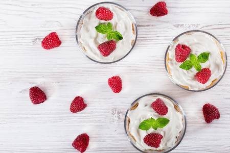 homemade yogurt in cups with whole grain cereals flakes and  raspberries, decorated with mint leaves on a wooden table, view from aboveの写真素材