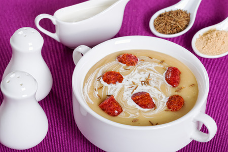 delicious Beer and cream spicy Soup with Kielbasa Sausage sprinkled with cumin in white soup cup on magenta table mat with salt and pepper shakers, authentic recipe, close-upの写真素材