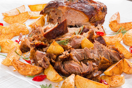 fried Potato wedges and Big Piece of Slow Cooked Oven-Barbecued Pulled Pork  shoulder, cooking according authentic recipe, on parchment paper with rosemary and pieces of chili, close-upの写真素材