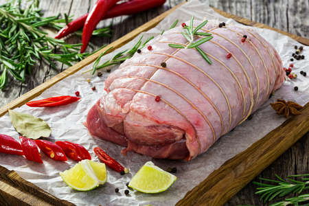raw turkey roulade preparing for grill with spices, bay leaf, lemon wedges, and chili pepper on chopping board, rosemary on wooden background, view from above,close-upの写真素材