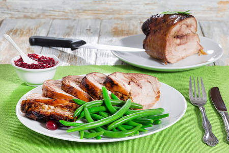 delicious roast in oven turkey roulade cut in slices with boiled green beans on white plate, berry sauce and whole piece of meat on wooden background, close-upの写真素材