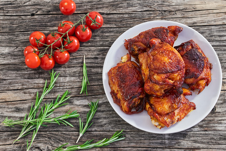 delicious fried chicken thigh marinated in mixture of honey, soy and oyster sauce and seasonings on white plate on old wooden table. cherry tomatoes and rosemary on background, view from aboveの写真素材