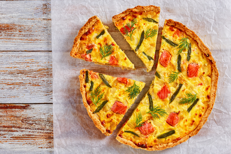 delicious homemade french quiche with red fish, green bean, sauce bechamel and Emmental cheese cut in slices on baking paper on white wooden background, view from aboveの写真素材