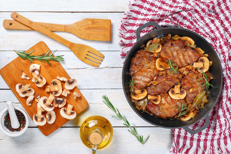 delicious Pork fillet stew with onion. mushrooms, rosemary, semi dry white wine and spices in iron stew pan on white table with wooden spatulas, easy recipe, view from aboveの写真素材