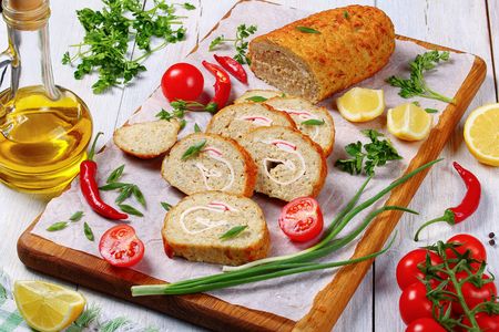 close-up of delicious baked in oven Gefilte minced white fish fillets roll-up with crab meat cut in slices on chopping board with scallions, fresh spring parsley, lemon, chili peppers, view from aboveの写真素材