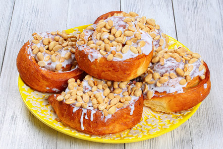 delicious freshly baked homemade cinnamon rolls topped with peanuts on plate on wooden table, view from above, close-upの写真素材