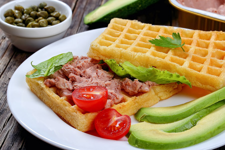 waffles sandwich with avocado, meat mushrooms and liver pate, lettuce, spinach, tomatoes on white plate on dark wooden table, view from above, close-up, macroの写真素材