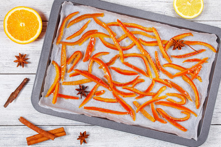 delicious sweet Homemade candied orange and lemon  peels cooked on baking sheet with cinnamon, nutmeg and anise star. half of orange and lemon on wooden table, view from aboveの写真素材