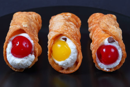 delicious homemade Sicilian Cannoli filling with ricotta cheese and cocktail cherries on black plate...