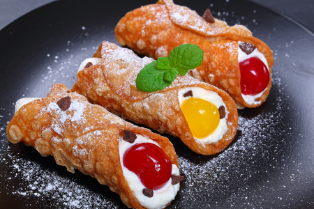 Sicilian Cannoli - traditional Italian Dessert, filling with ricotta cheese and cocktail cherries, sprinkled with powdered sugar on black plate, authentic classic recipe, view from above, close-upの写真素材