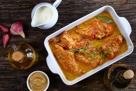 appetizing Rabbit Cooked with Dijon Mustard and white wine or lapin a la moutarde in gratin dish on old dark wooden table with ingredients on background, authentic french recipe, view from aboveの写真素材