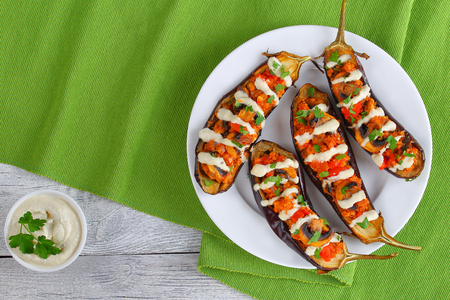 delicious baked Eggplants Stuffed with Quinoa, mushrooms, tomatoes and Tahini Sauce drizzled over, healthy and easy vegan mediterranean recipe,sesame sauce in bowl on wooden boards, view from aboveの写真素材