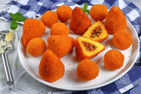 sicilian arancini - saffron risotto cones and balls stuffed with meat ragu and green peas on platter...