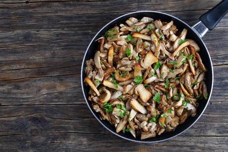 delicious flavor Side dish - Funghi trifolati or fried Boletus mushrooms sprinkled with finely chopped parsley on skillet on old dark wooden table, view from above, close-upの写真素材