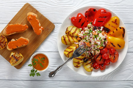 delicious salad of shrimps, octopus, calamari, mussels served with grilled vegetables on white plate on wooden table. toasts with paprika mayonnaise on cutting board, view from aboveの写真素材