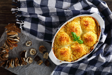 potato polenta vegetarian polpette stuffed with mushrooms ragout and baked in oven with creamy cheese and parsnip sauce in baking dish. dried porcini and kitchen towel at background, view from aboveの写真素材