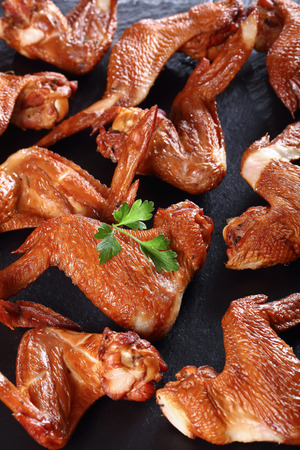 delicious crispy smoked chicken wings on a black stone plate on wooden table, vertical view from above, close-upの写真素材