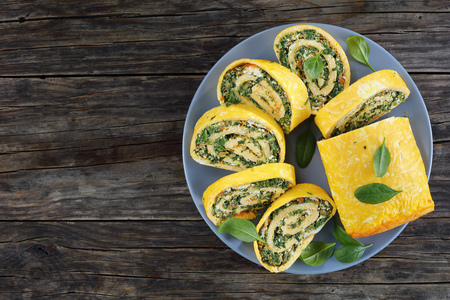 delicious egg roulade with a soft filling of mix of spinach, feta and carrots cut in slices on grey plate on dark wooden table, view from aboveの写真素材