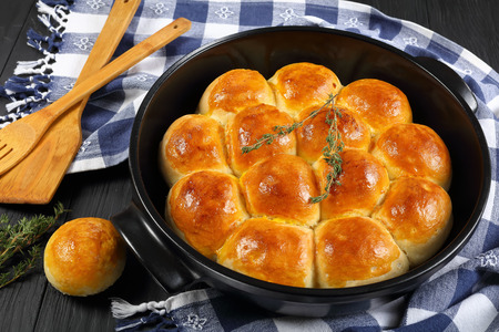 delicious freshly baked golden brown soft and fluffy homemade dinner rolls in baking dish with kitchen towel and spatulas on wooden kitchen table, view from above, close-upの写真素材